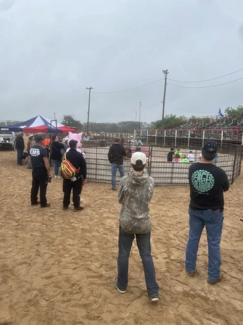 Spectators watching the hog-catch pen from inside the arena, with the pig mascot and Texas-flag tent in the background.